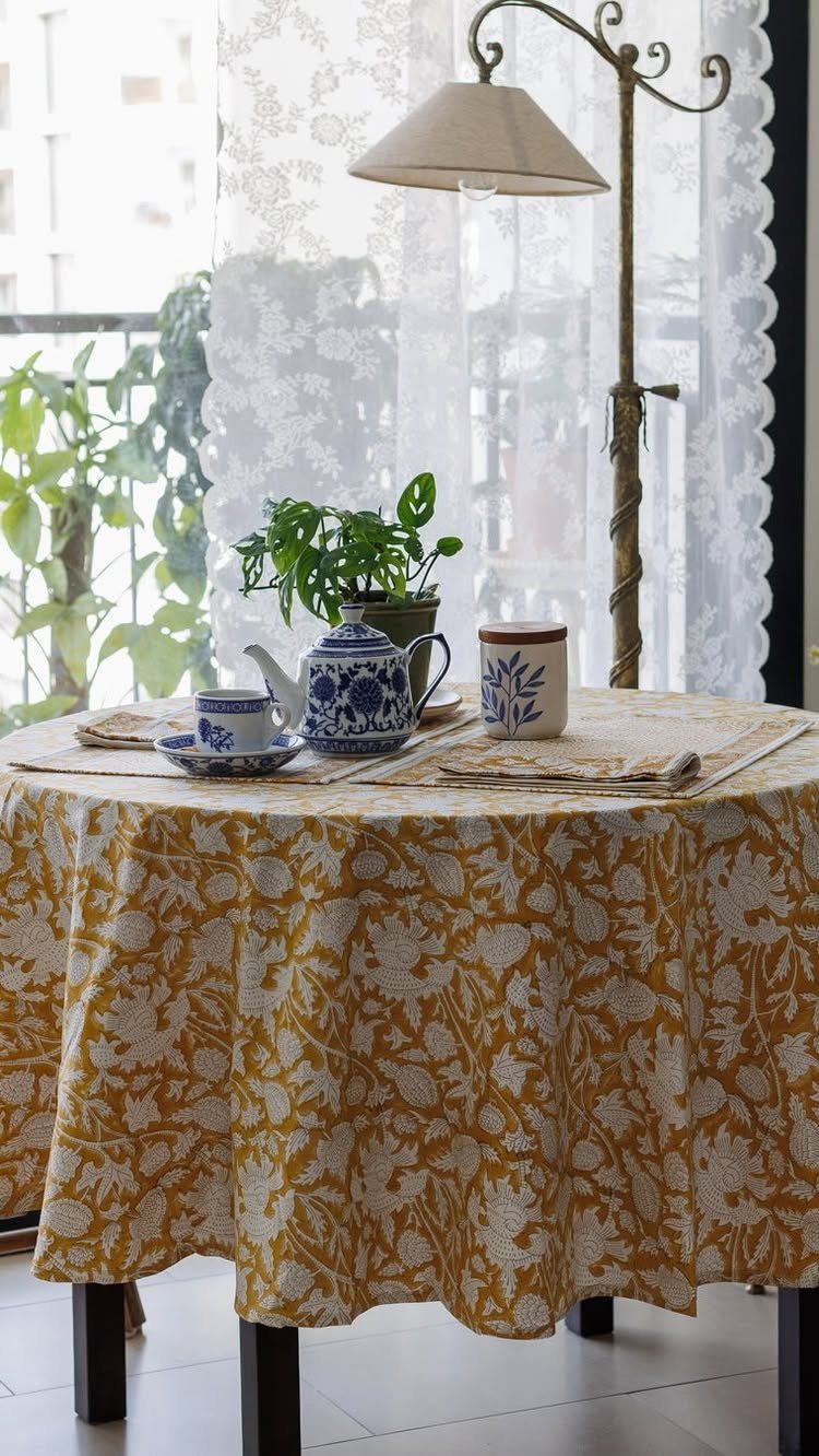 10 Dining Room Colors for 2027 That Feel Fresh and Grounded 2 Round dining table with a mustard yellow floral tablecloth, teapot, and potted plant.