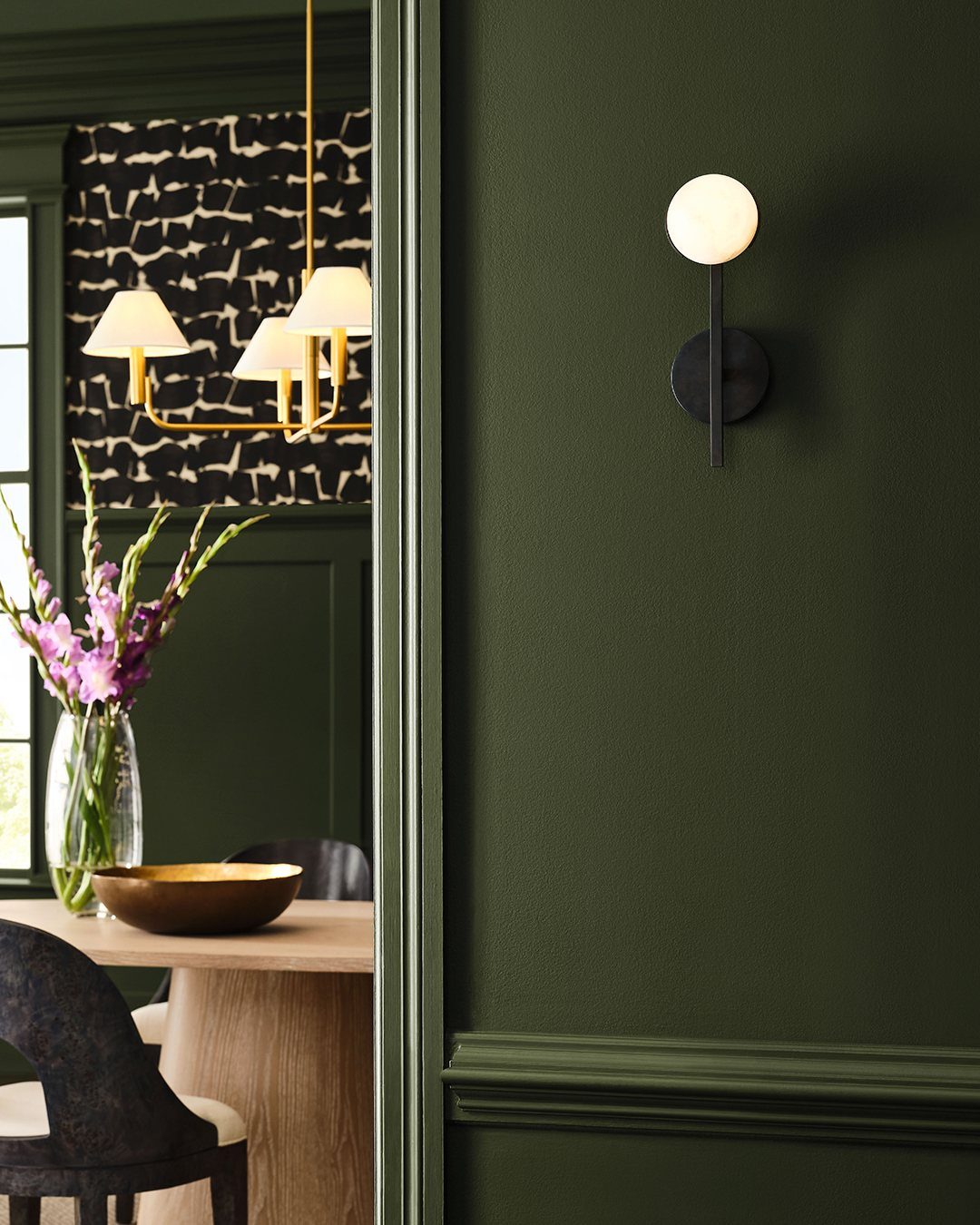 10 Dining Room Colors for 2027 That Feel Fresh and Grounded 1 Deep forest green dining room walls with a wooden table and globe wall sconce.