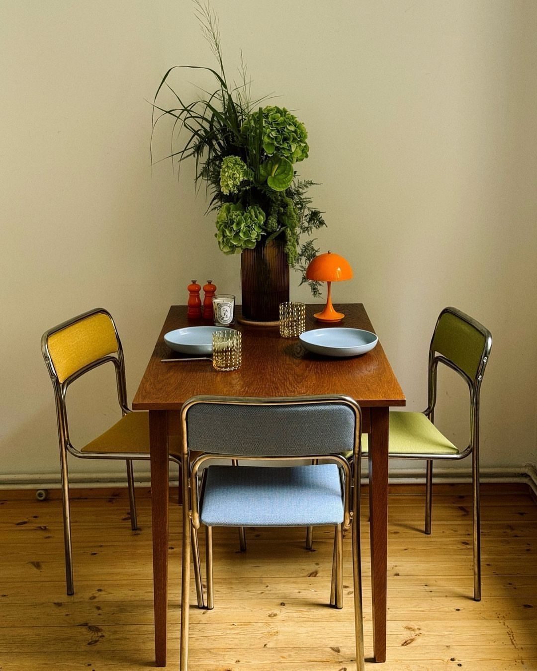 15 Dining Room Decor Modern Ideas with Style and Function 3 Wooden dining table surrounded by mismatched yellow, blue, and green chairs with greenery.