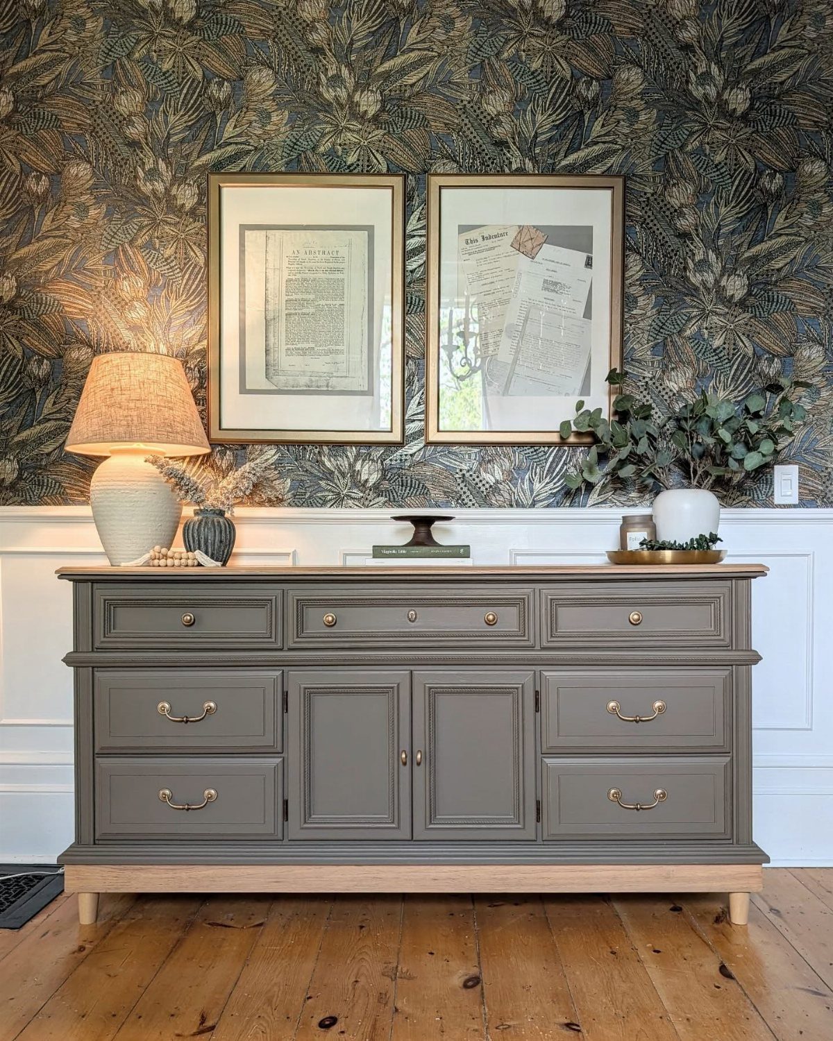 15 Dining Room Decor Modern Ideas with Style and Function 11 Grey wooden sideboard against botanical wallpaper with framed art and a table lamp.