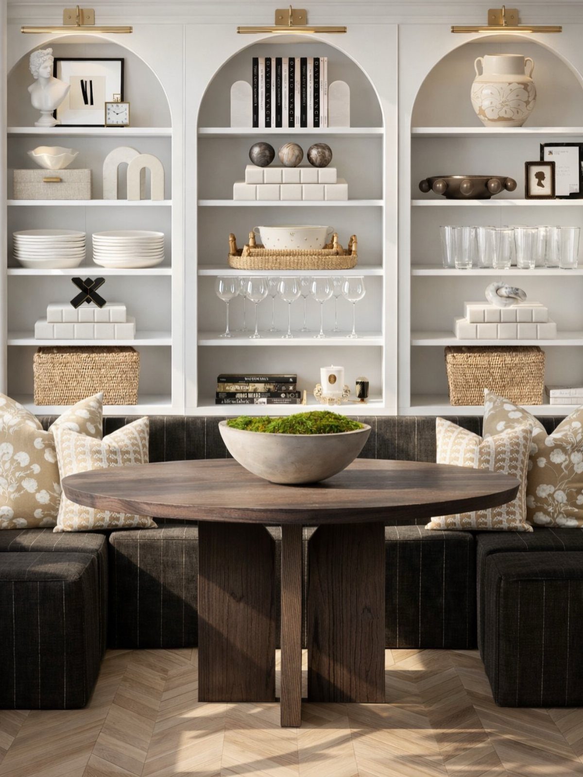 Round dark wood dining table with white built-in arched shelving units and gold lighting.