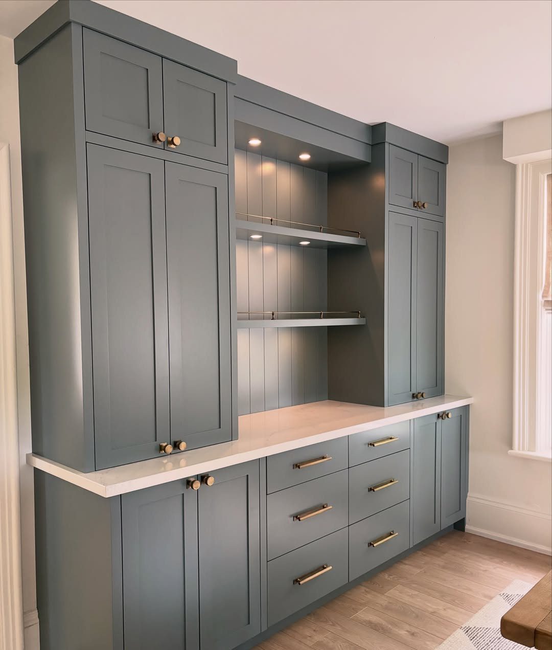 Blue-grey built-in cabinetry with white countertops and recessed shelving in a dining area.