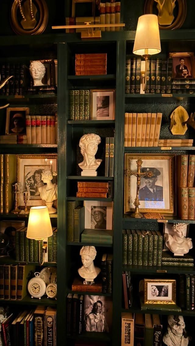 Dark green bookshelves filled with vintage books, classical busts, and framed old photographs.