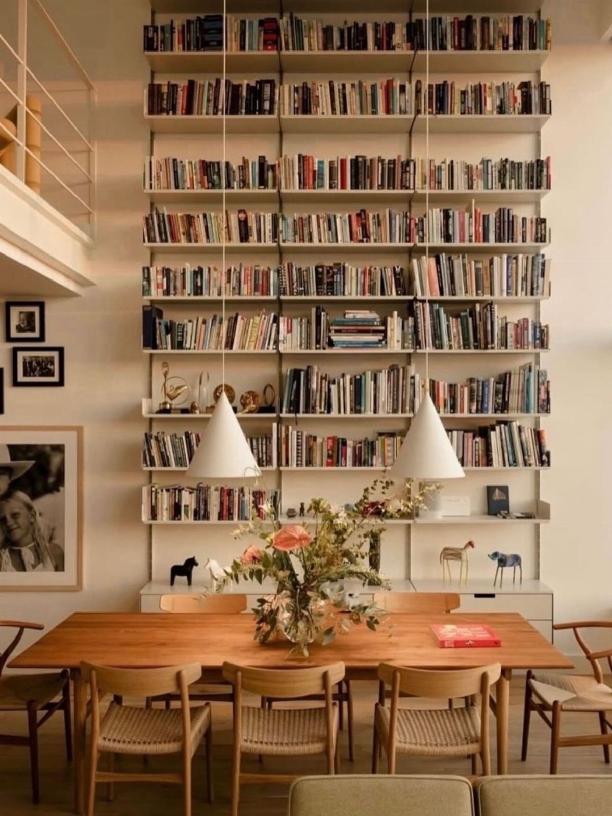 Tall white floor-to-ceiling bookshelves filled with books behind a wooden dining table.
