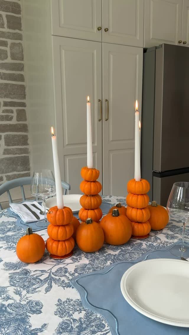 White taper candles held up by stacks of small orange pumpkins on a table