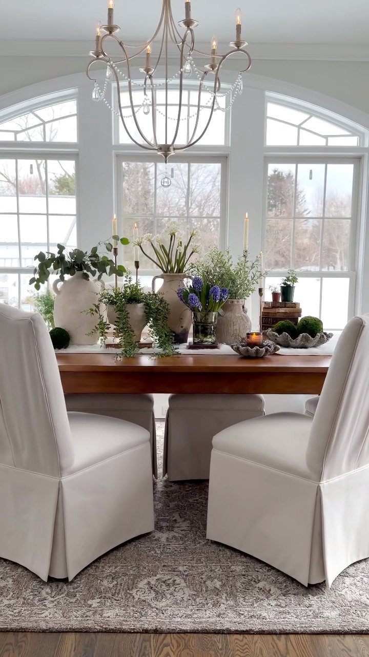 Wooden dining table with a greenery centerpiece of vases and blue flowers.