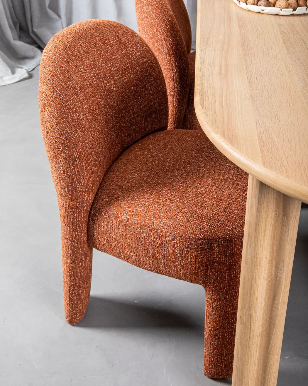 Textured orange fabric chair paired with a smooth light wood dining table.