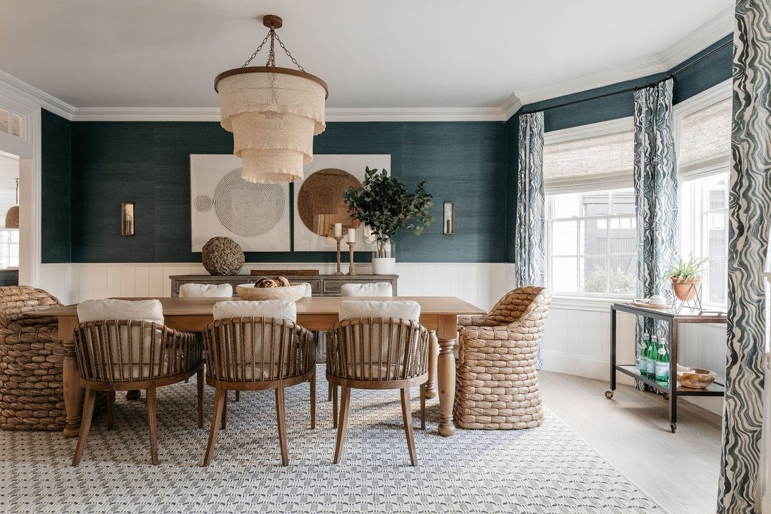 Wooden dining table with a mix of wicker and slat-back chairs in a teal room.