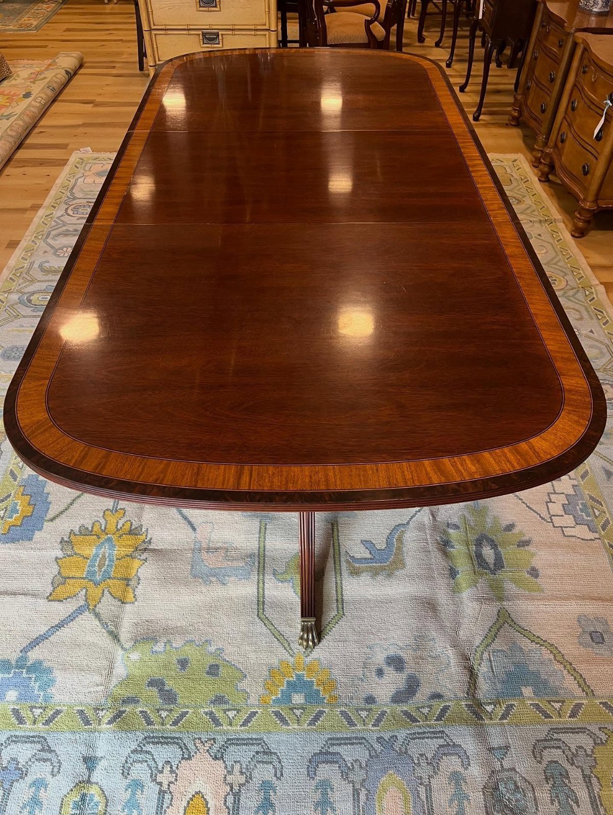 Dining Room Table for 12: 3 Handcrafted Options 2 Polished dark brown wooden dining table with oval top on a patterned rug.