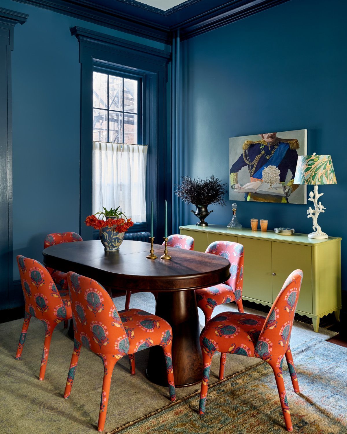 Dining room with blue walls, orange chairs, and a military themed painting.