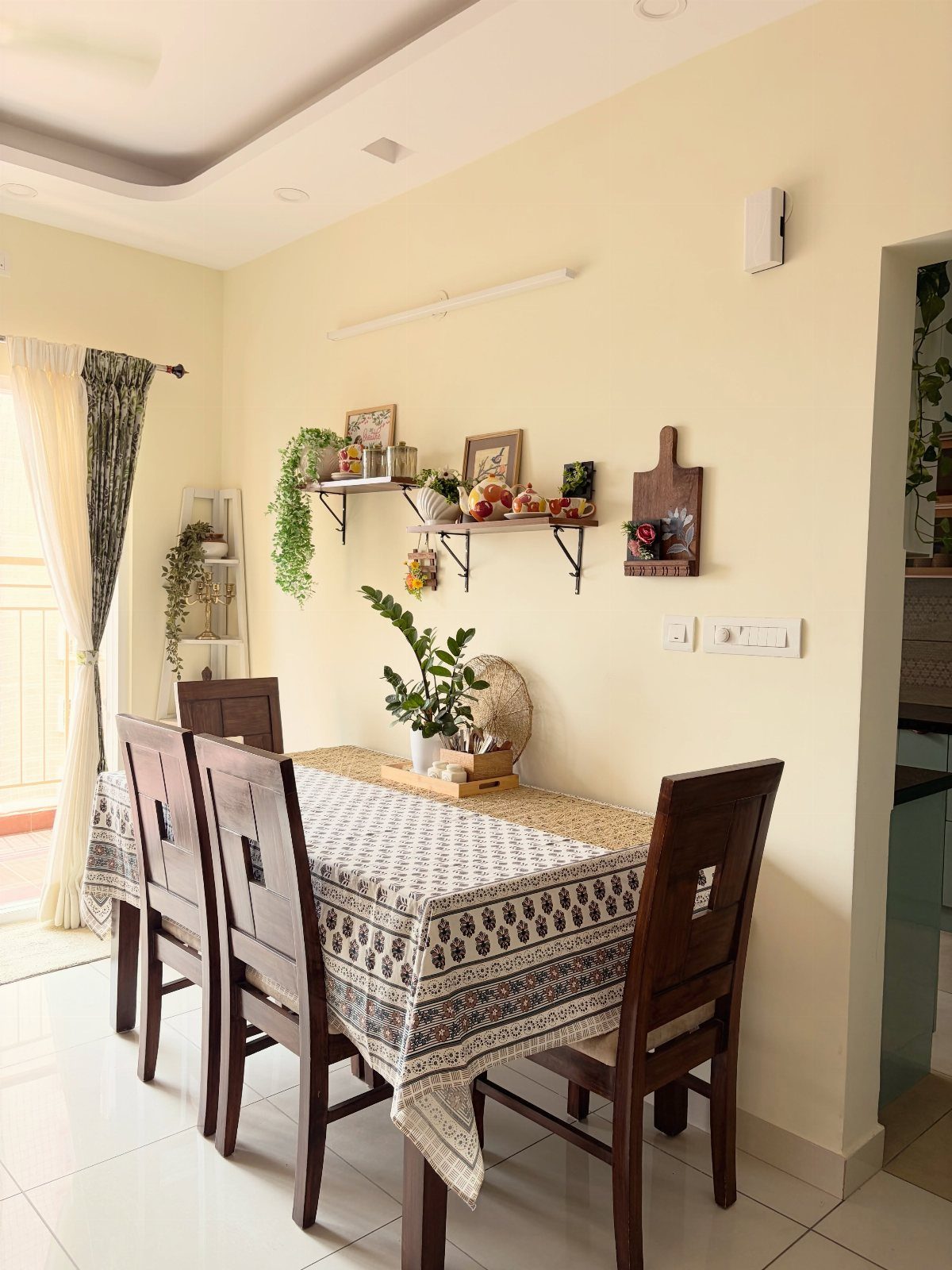 Dining room with patterned tablecloth and decorative wall shelves with plants and frames