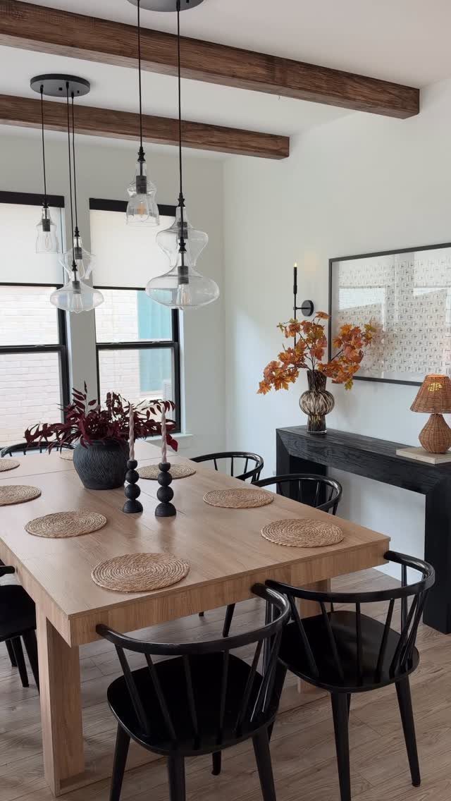 Dining room with wood ceiling beams, light wood table, and autumn floral decor.