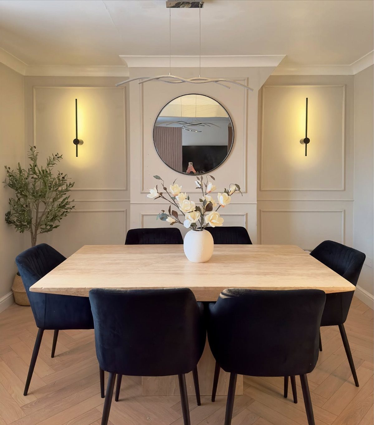 Dining room with wall molding, a round mirror, and glowing vertical wall sconces.