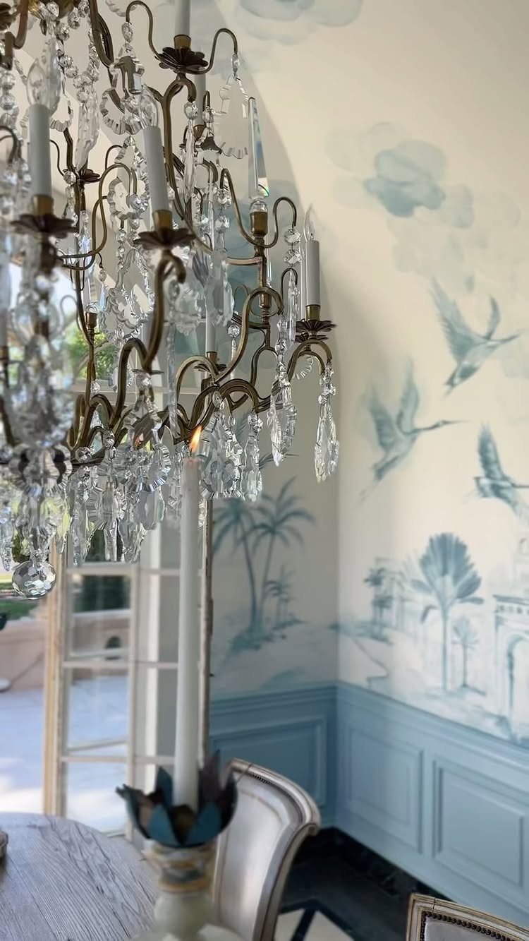 Crystal chandelier in front of a blue and white scenic wall mural with birds.