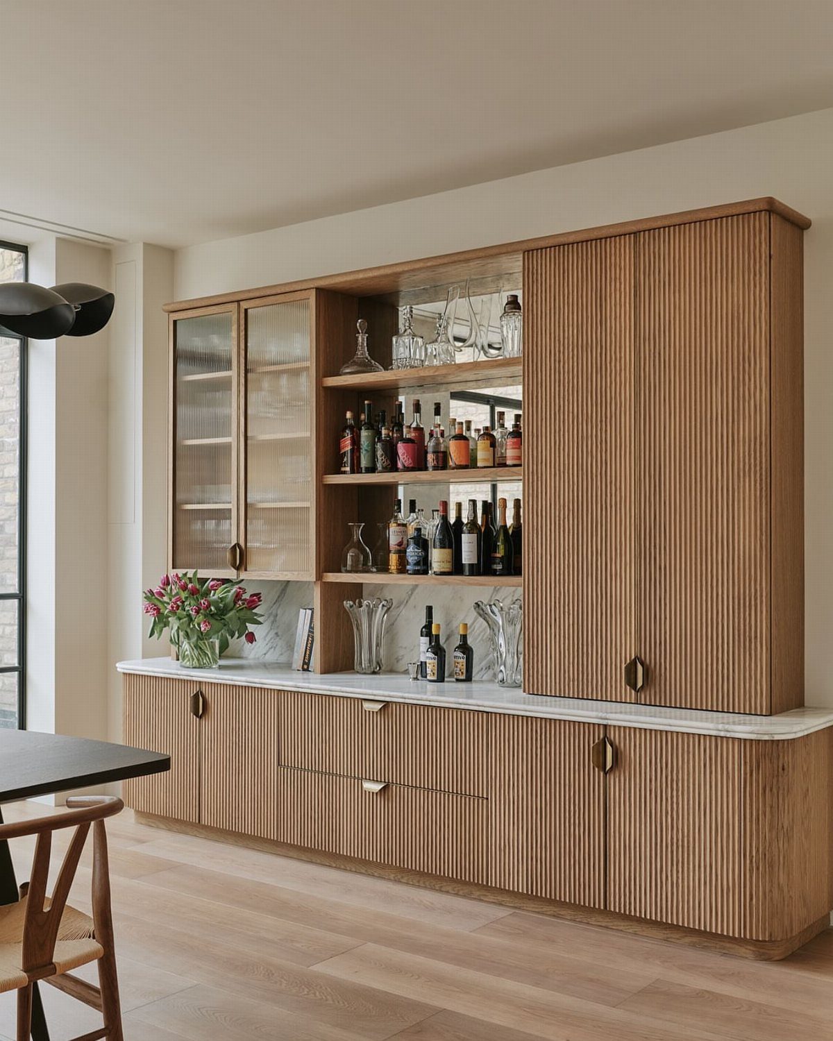 Light wood fluted sideboard with marble top and integrated spirits display cabinet.