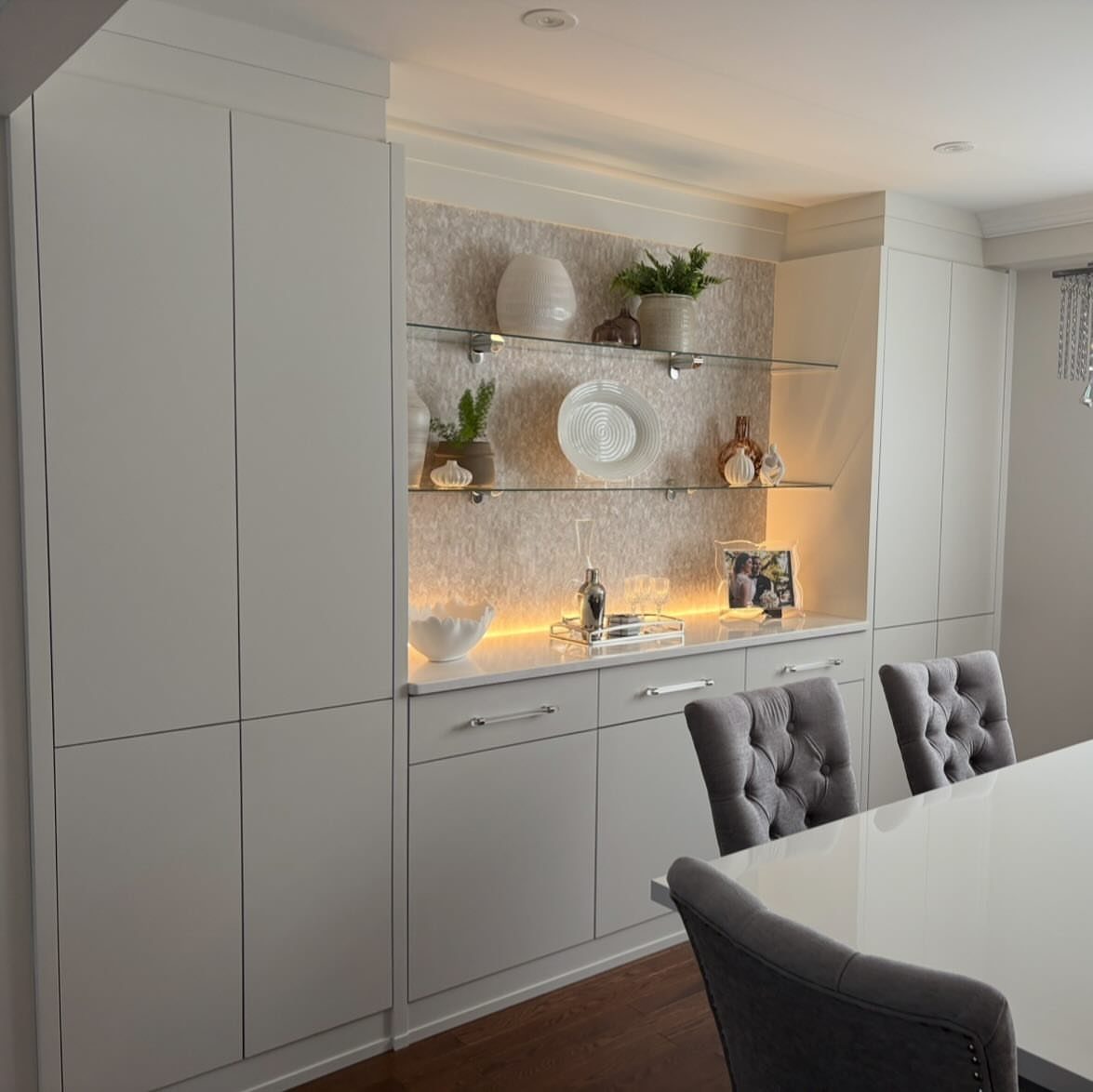 White built-in buffet with glass shelves and integrated lighting in a dining room.