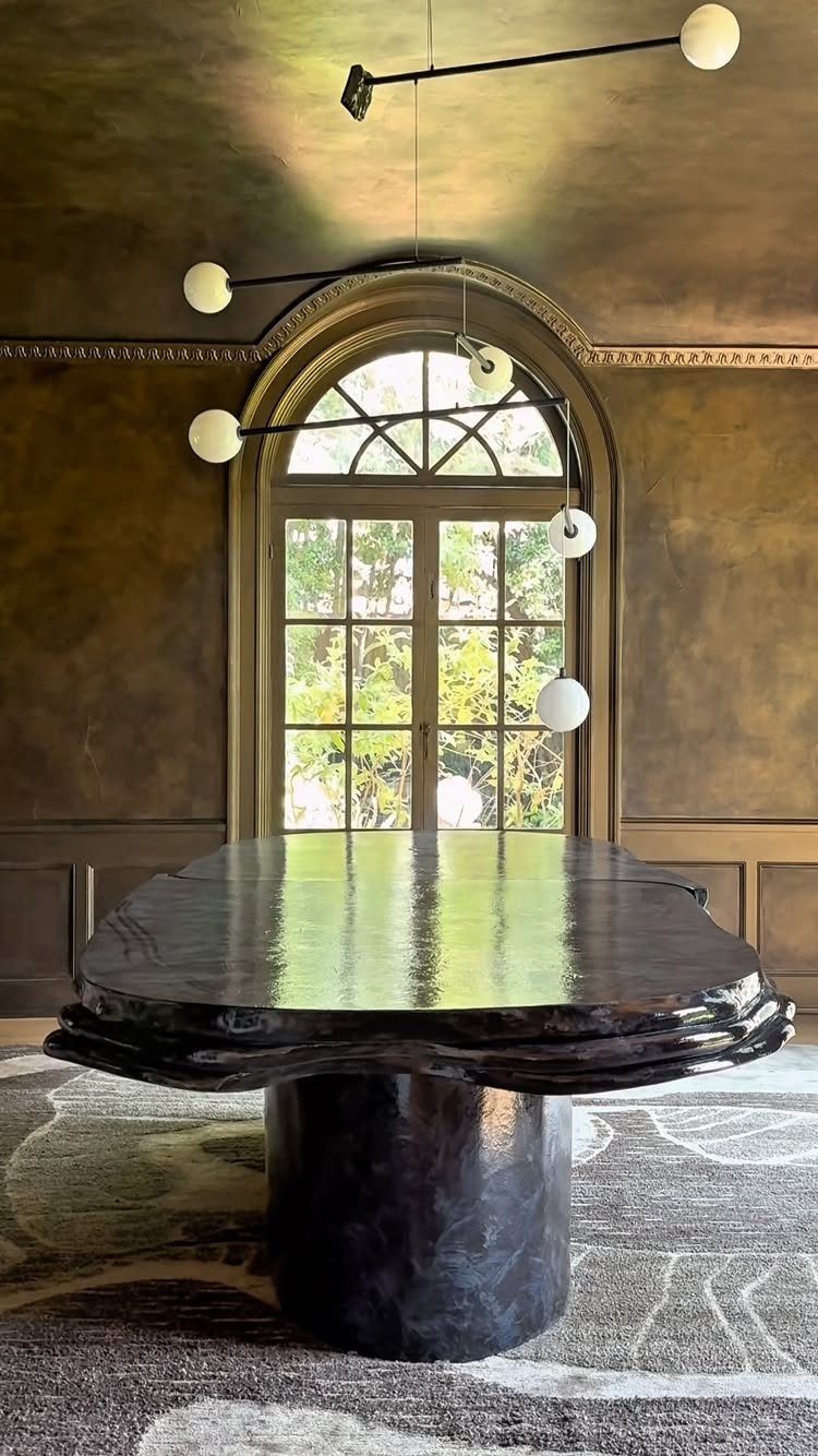 10 Dining Table in Living Room Ideas for Small Spaces 5 Organic black polished dining table in a room with gold walls and arched window