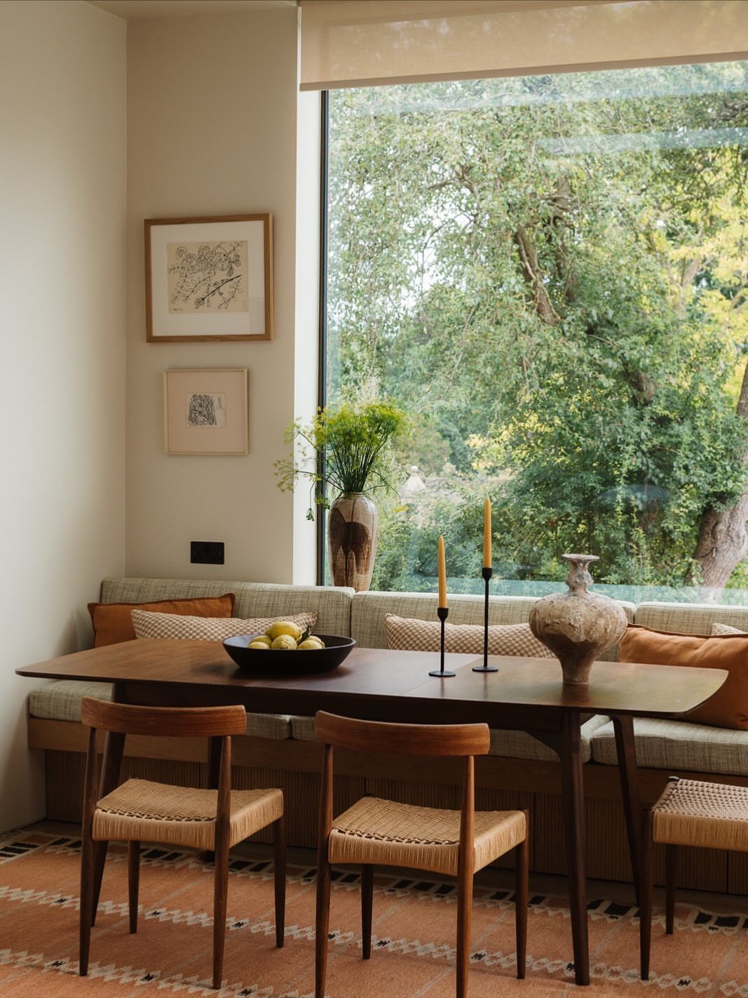 11 Dining Table Ideas for Small Spaces That Maximize Room 2 Wooden dining table with a built-in banquette seat and woven chairs by a window.