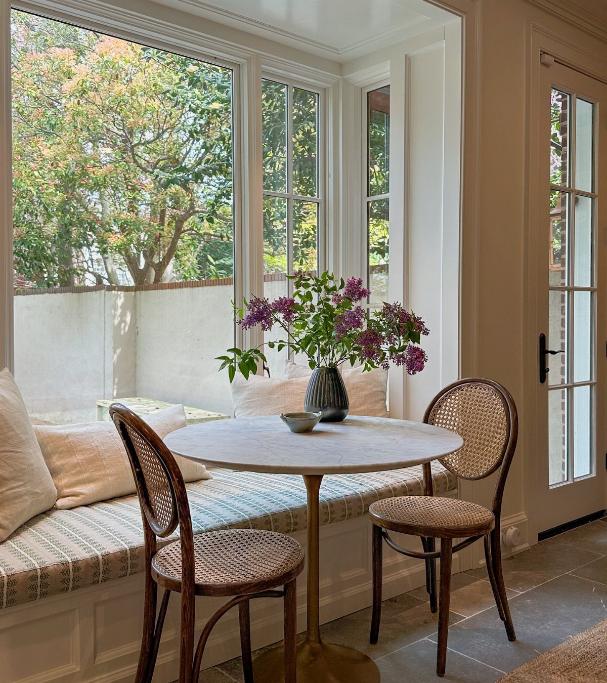 11 Dining Table Ideas for Small Spaces That Maximize Room 4 Small round marble bistro table with cane chairs by a sunny window seat.