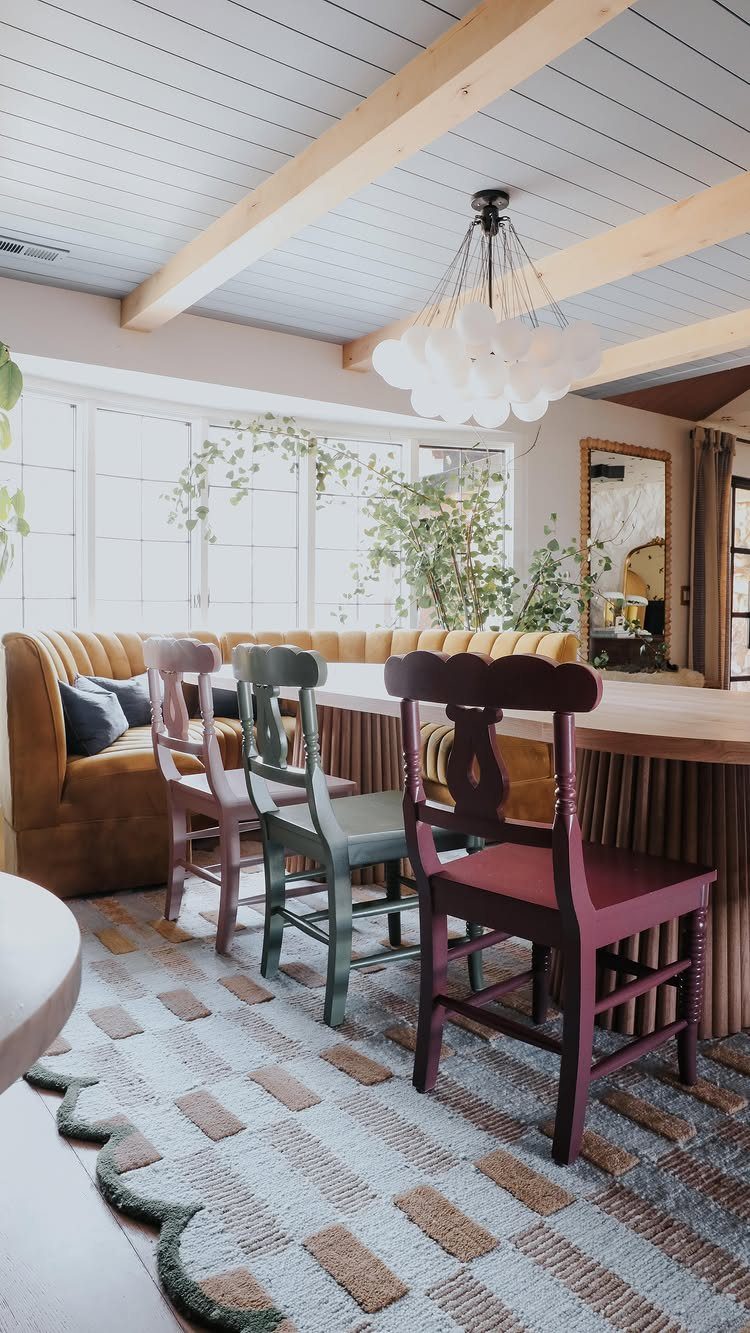 7 Dining Table with Mismatched Chairs Ideas That Work 4 Wooden dining table with mismatched pink, green, and burgundy chairs and yellow banquette.