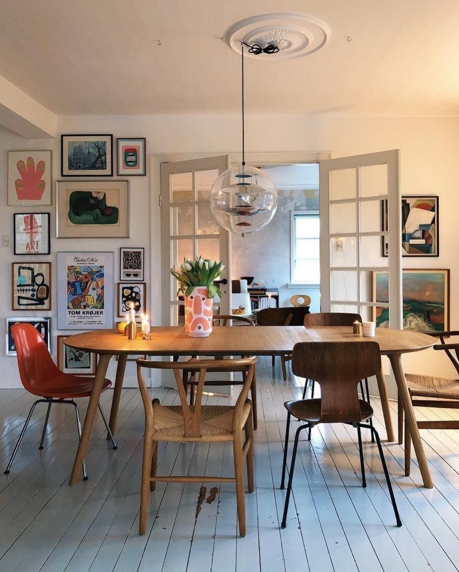 7 Dining Table with Mismatched Chairs Ideas That Work 6 Wooden dining table with mismatched orange, cane, and dark wood chairs in art-filled room