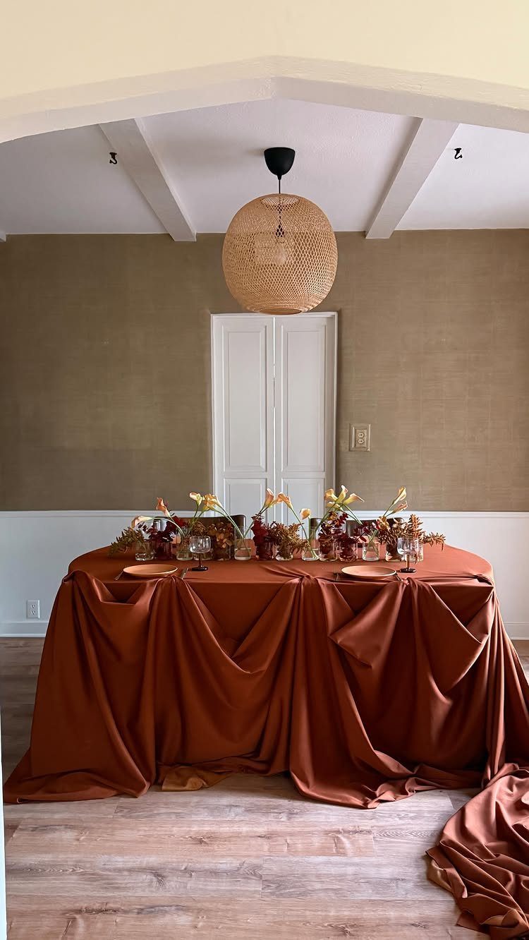 Rust-orange satin draped dining table with gold plates and autumn floral centerpieces.