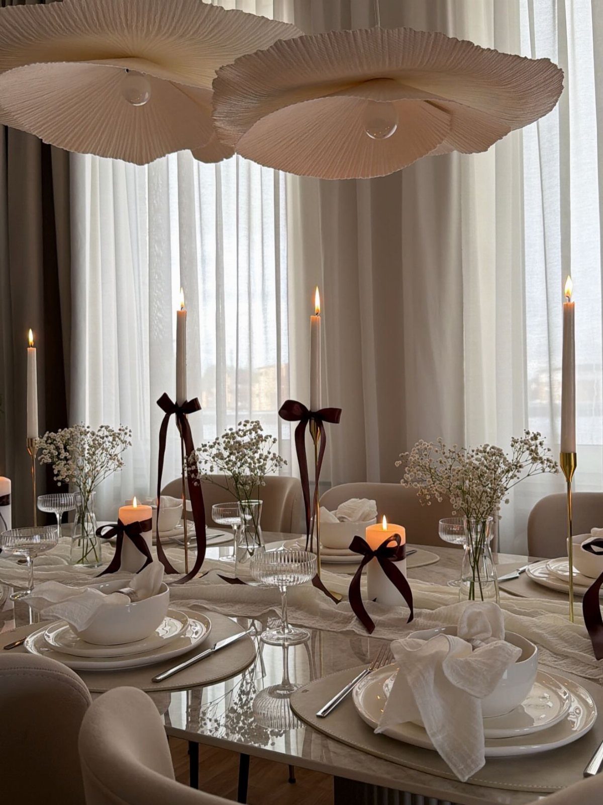 Elegant dining table set with white tableware, crystal glasses, and lit candles.