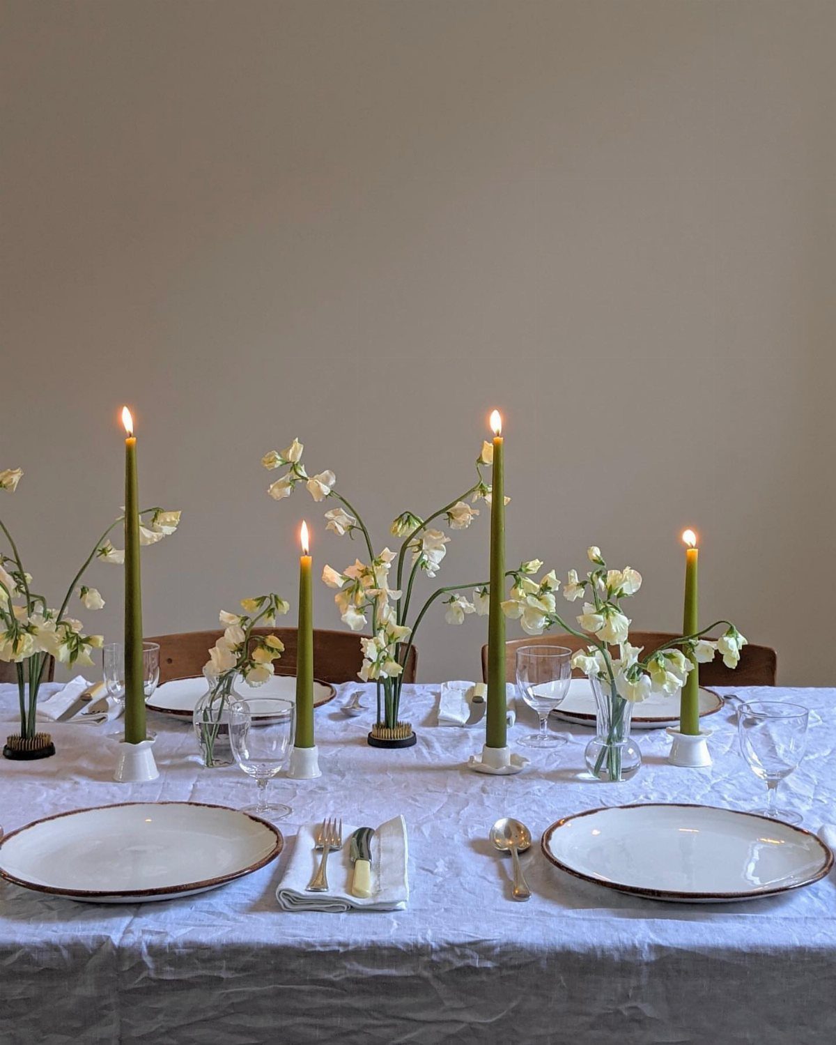 Dining table set with white linens, green taper candles, and white floral arrangements.