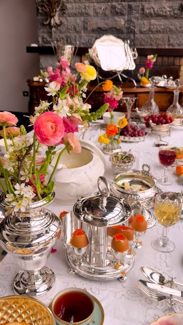 Silver vases with colorful flowers and vintage tableware on a white lace tablecloth.