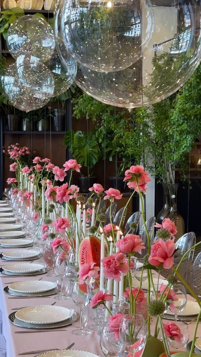 Dining table with pink flowers, white candles, and clear balloons in a lush setting