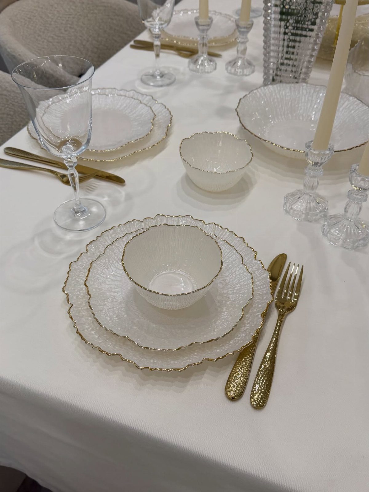 White textured dinnerware with gold rims and gold cutlery on a white tablecloth
