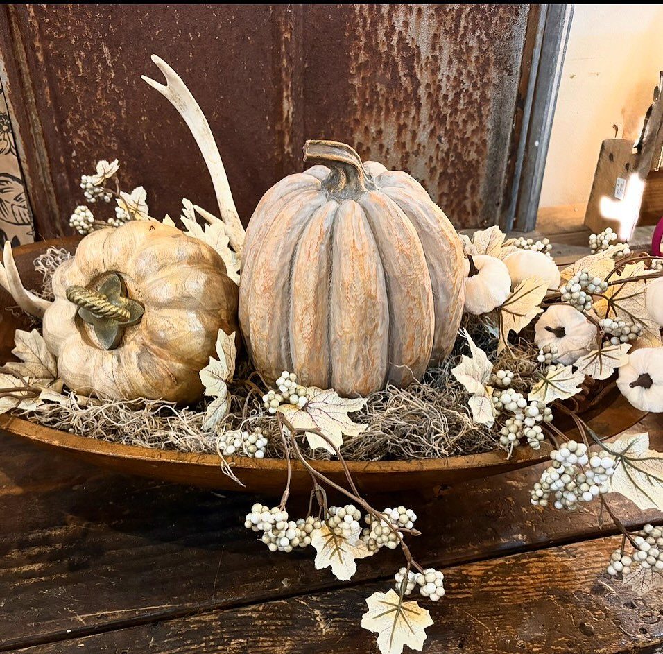 Wooden dough bowl filled with pumpkins, an antler, and autumn foliage on rustic wood.
