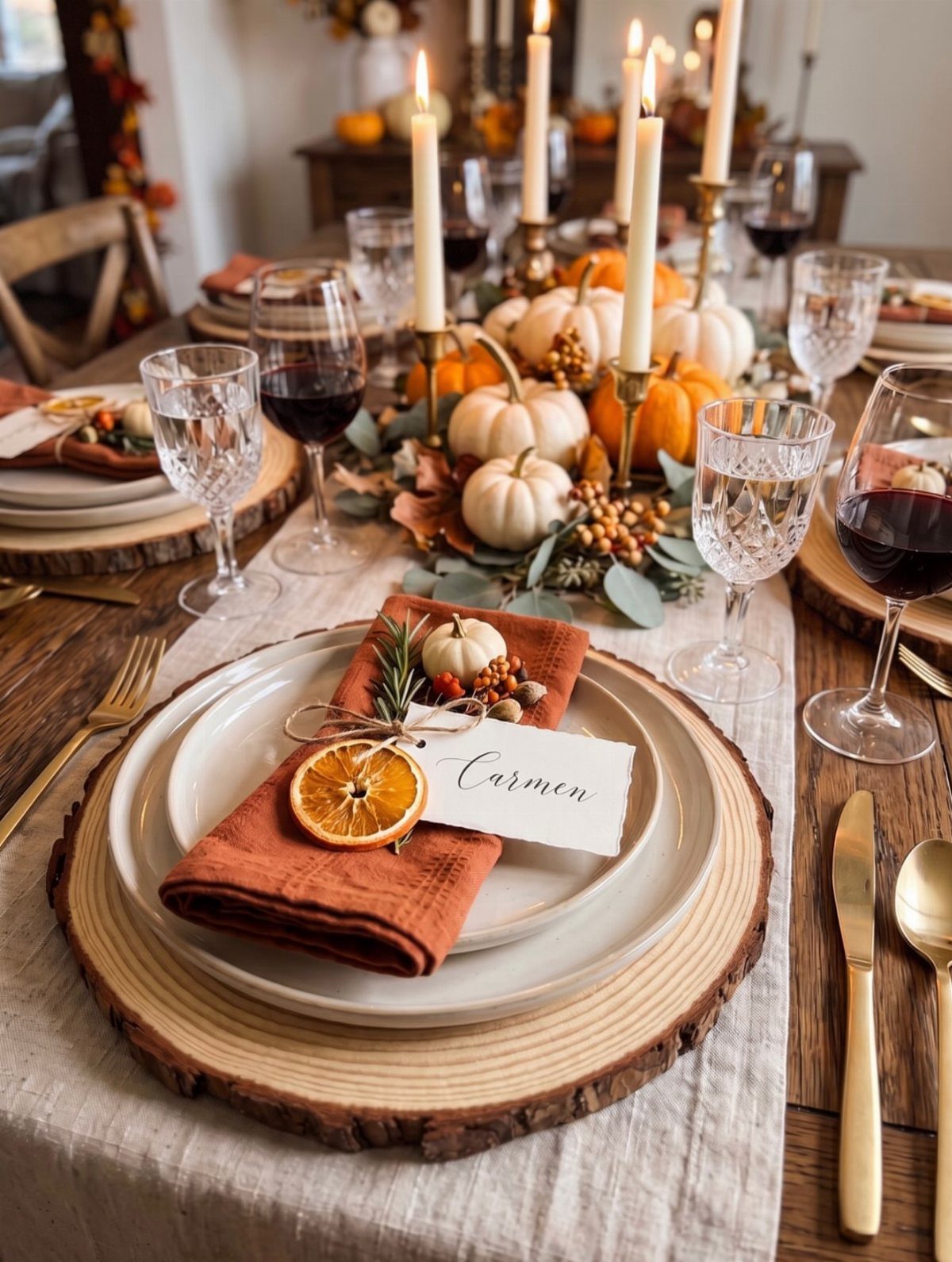 Fall dining table with wood chargers, orange napkins, pumpkins, and tall white candles.