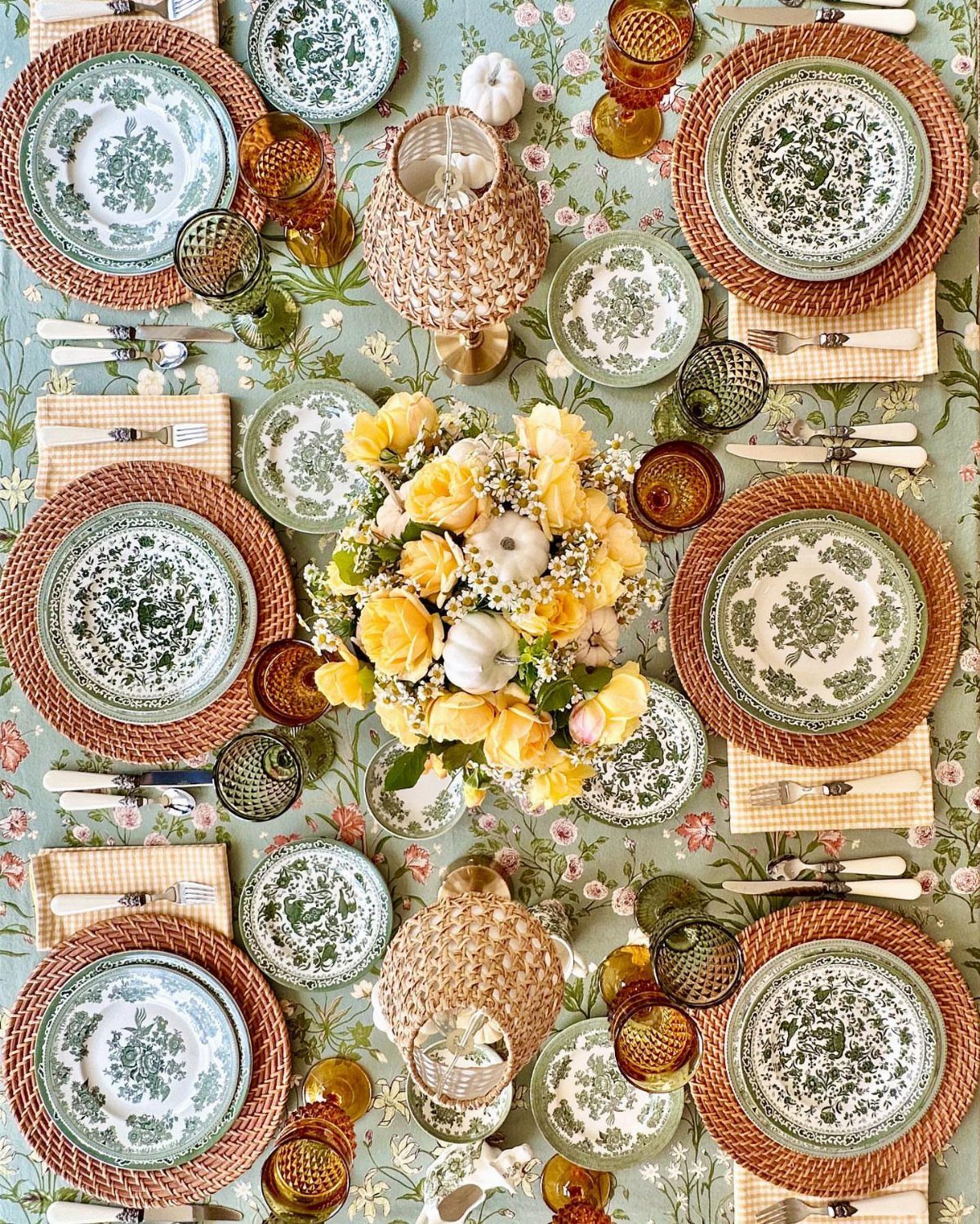 Fall dining table set with mixed patterned plates, amber glasses, and yellow roses.
