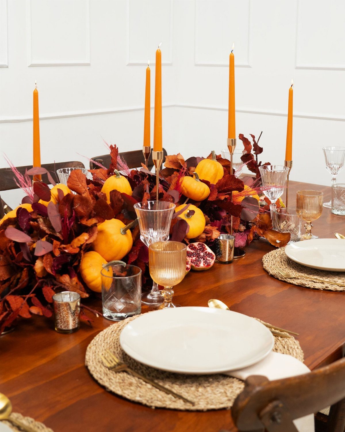 Small orange pumpkins and red autumn leaves arranged as a dining table centerpiece.