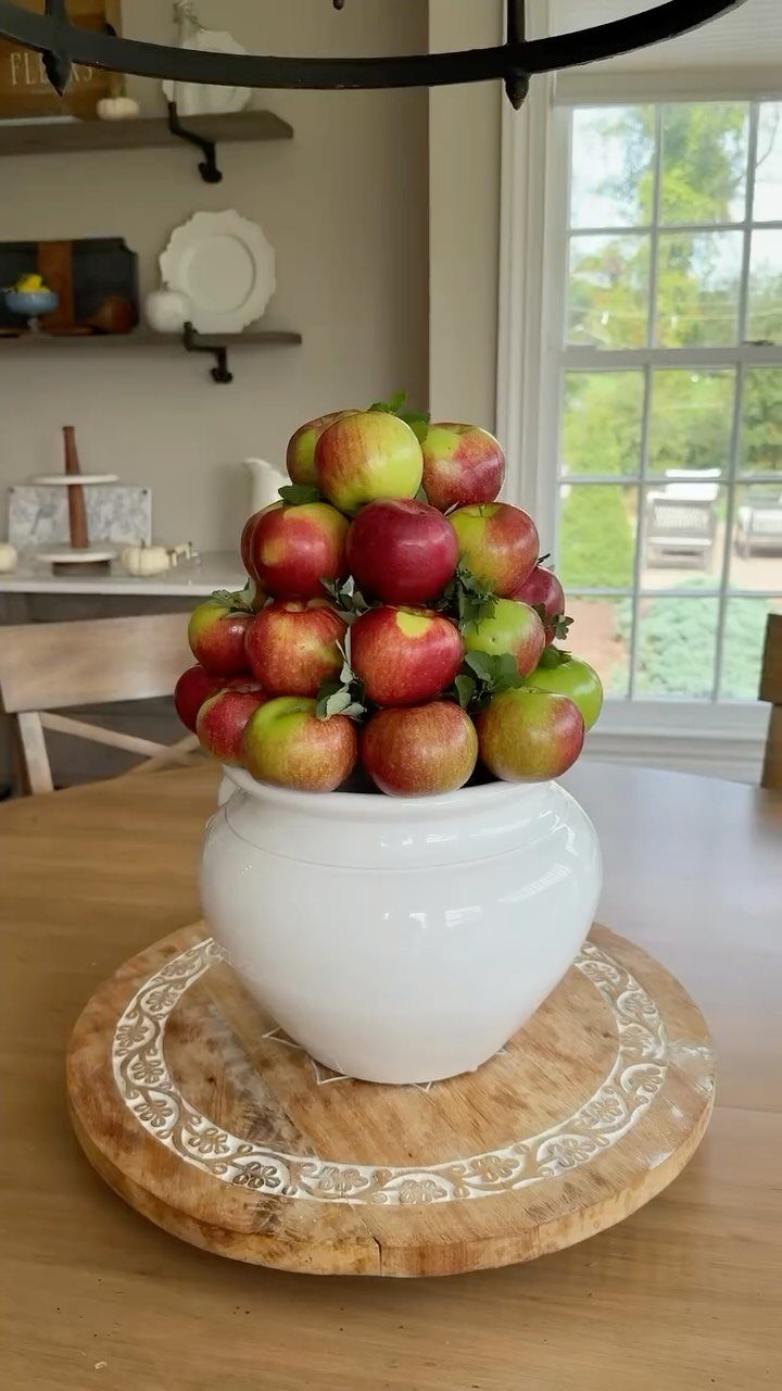 Red and green apples piled in a white bowl on a wooden platter.