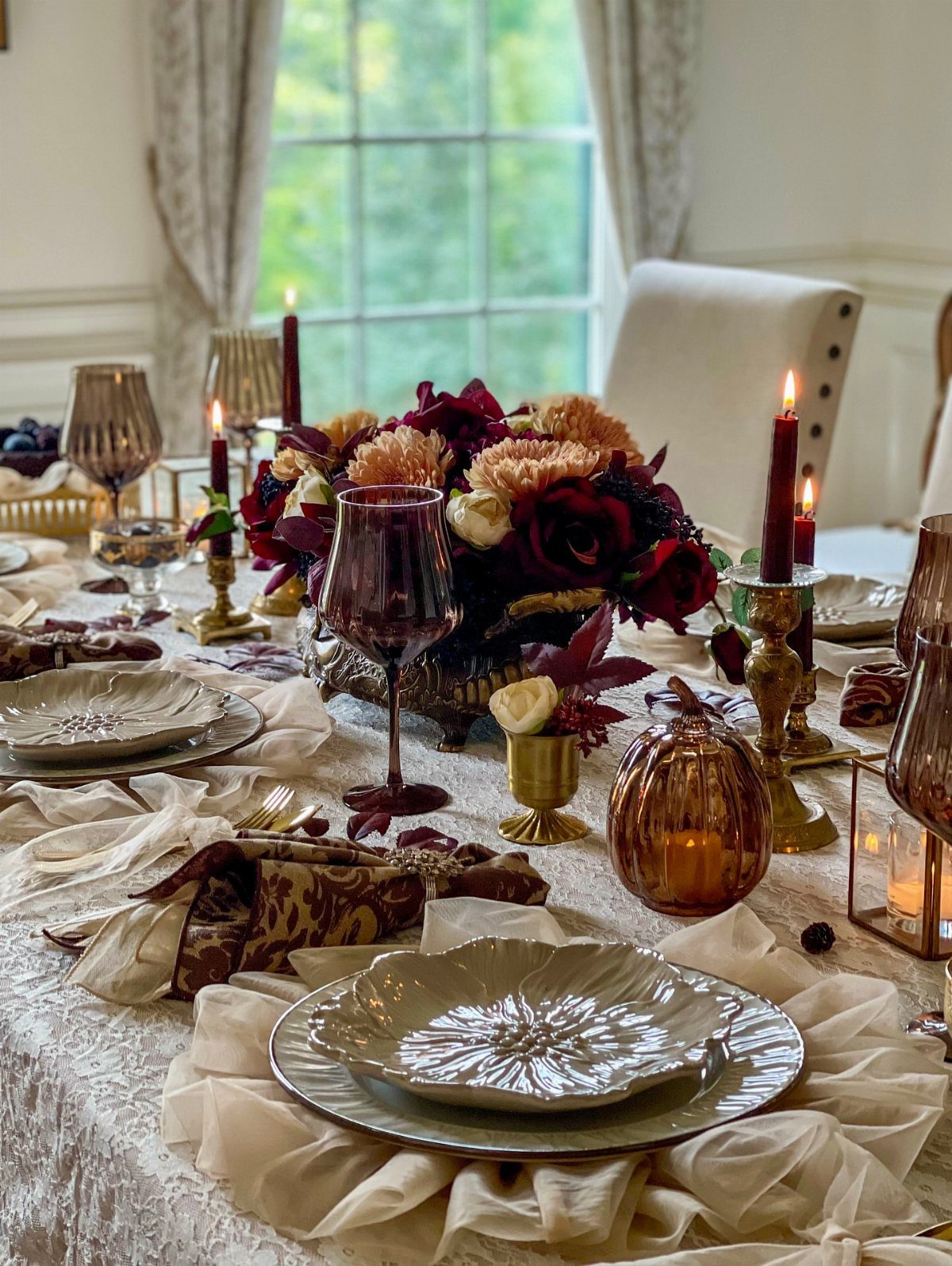 Moody fall tablescape with dark red flowers, burgundy candles, and cream ruffled plates.