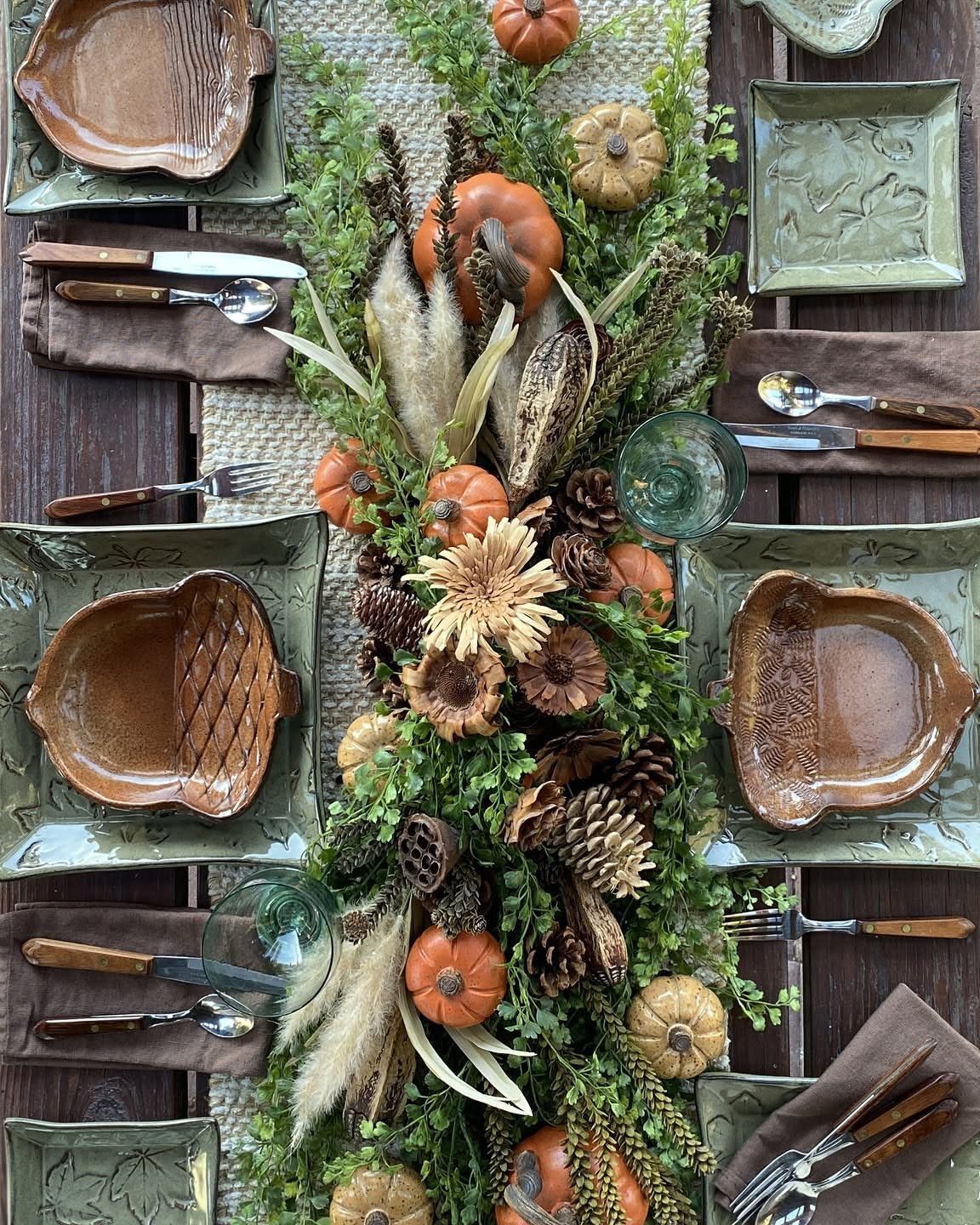 Fall dining table with a green garland centerpiece featuring pumpkins and pinecones.