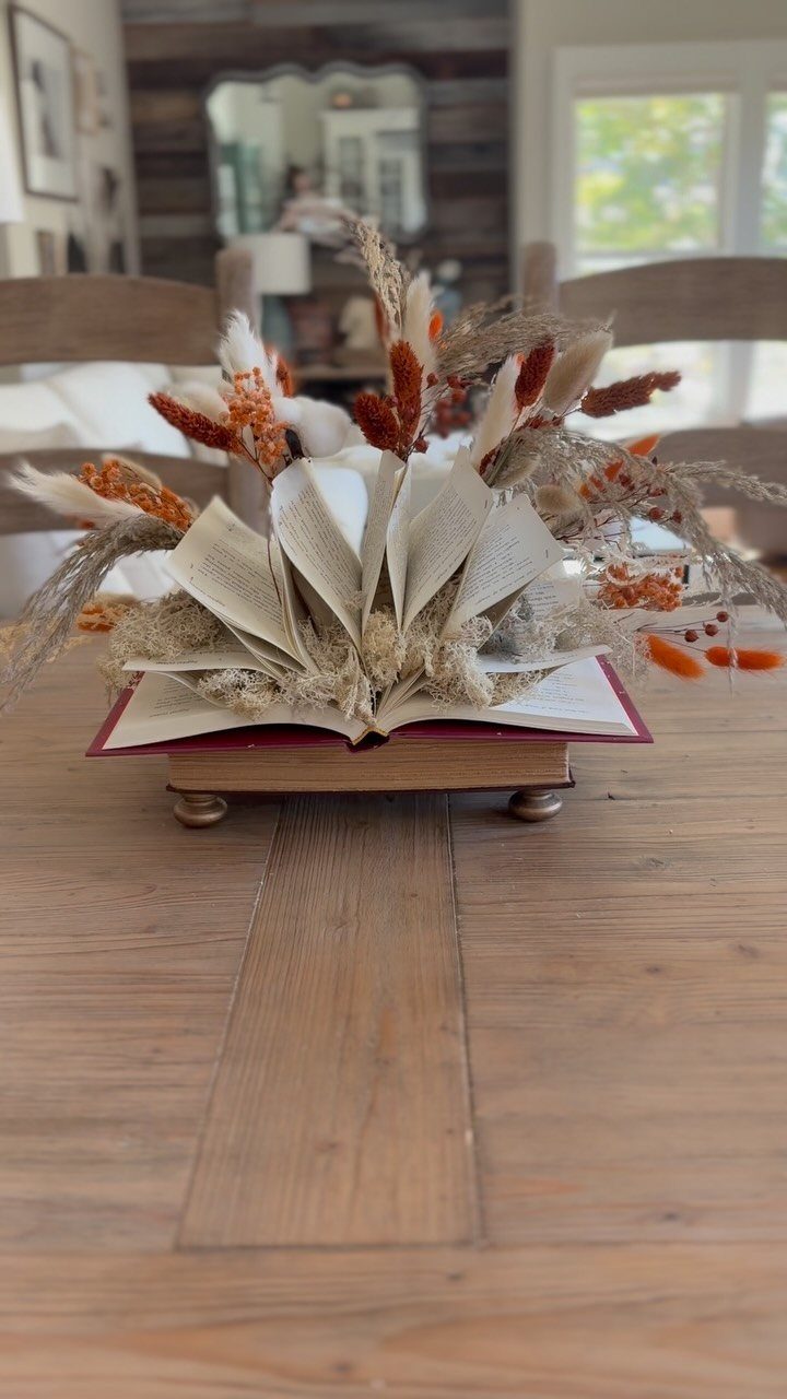 Dried flowers and grasses emerging from an open book on a wooden table.
