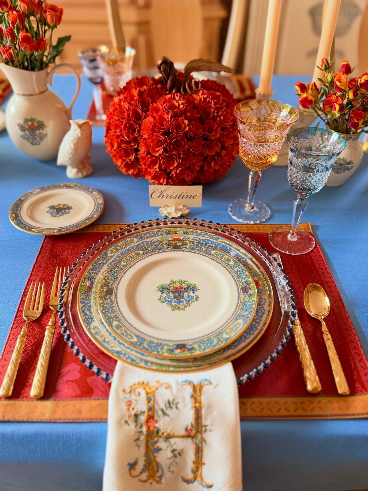 Red rectangular placemat with stacked decorative plates and gold cutlery on blue tablecloth.