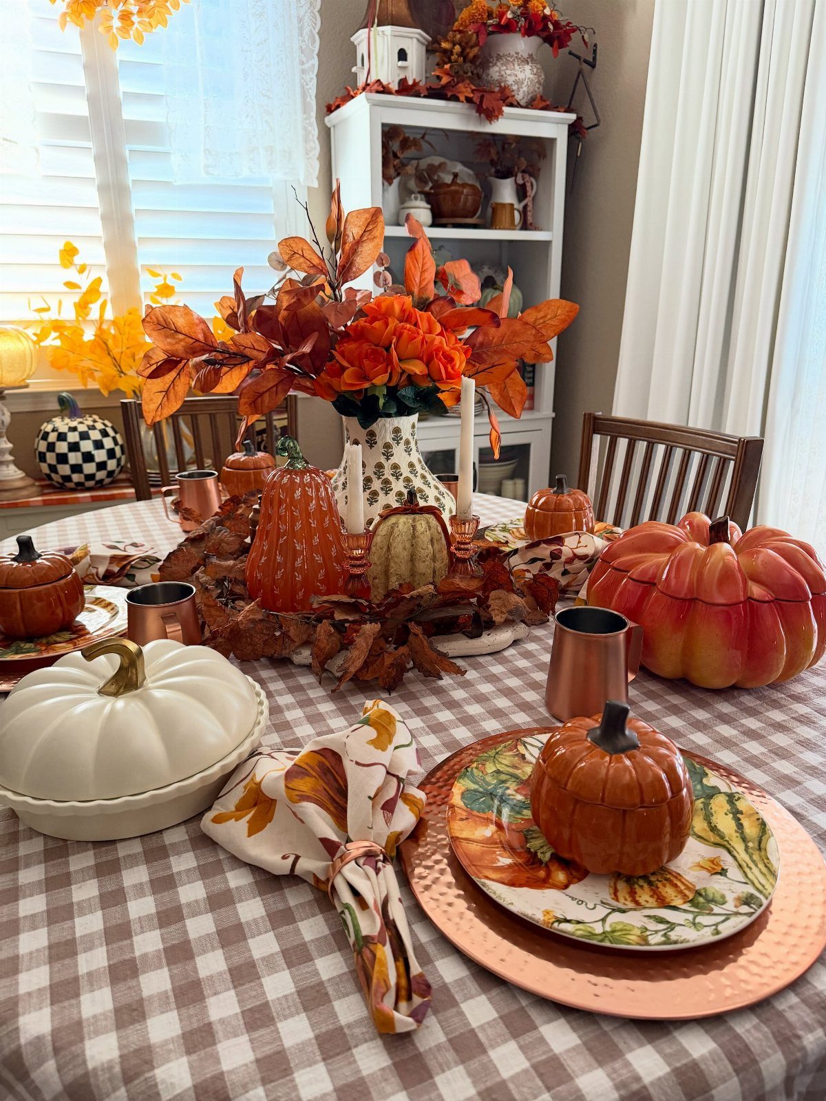 Fall dining table with pumpkins, autumn leaves, and copper plates on checkered tablecloth