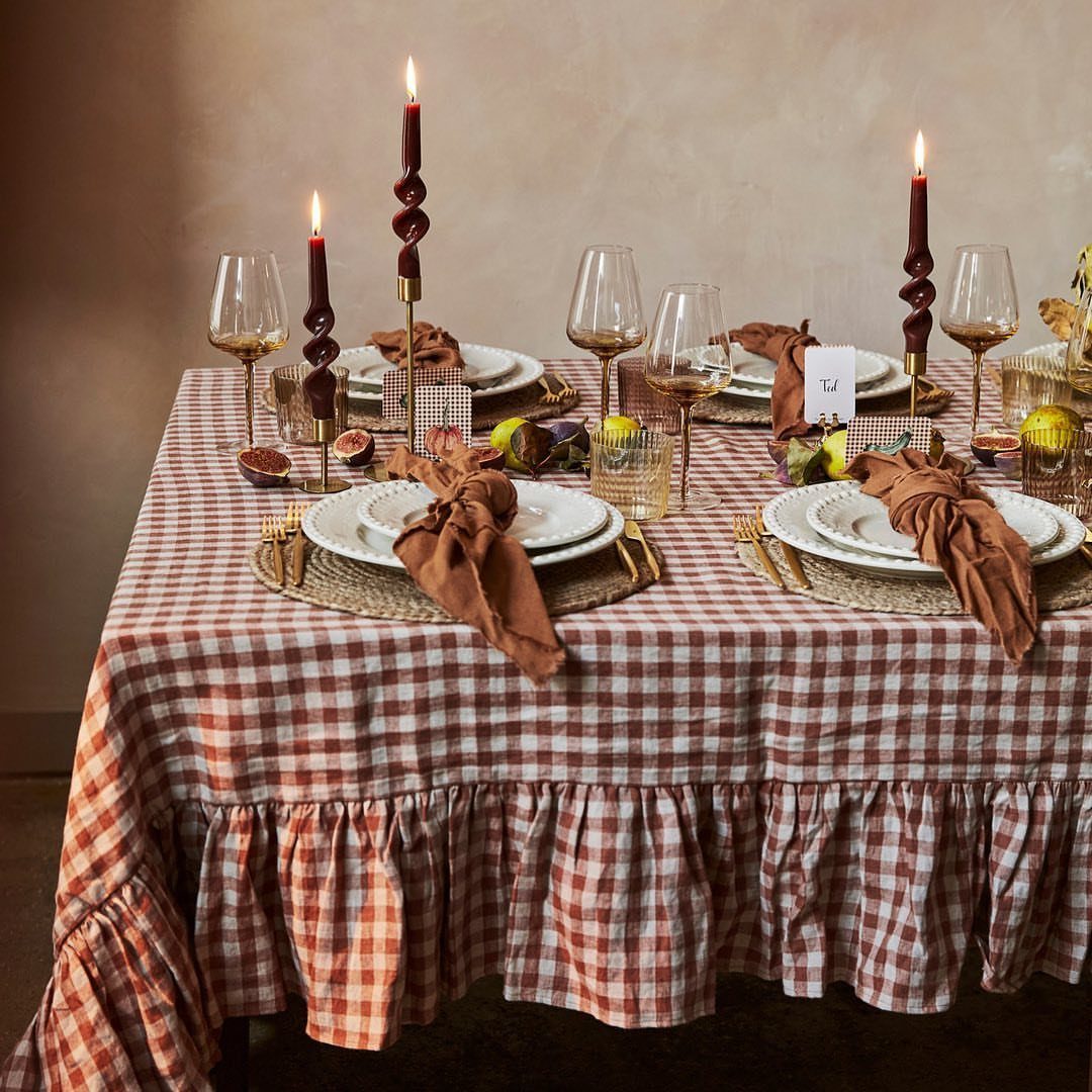 Dining table with red checkered cloth, white plates, brown napkins, and red candles.