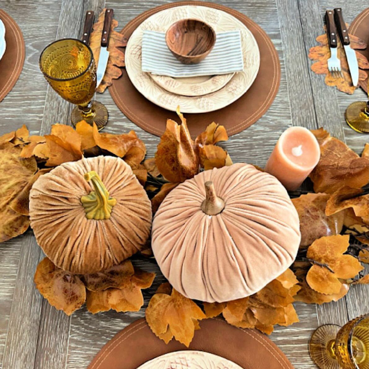 Velvet pumpkins and autumn leaves decorating a rustic wooden dining table setting.