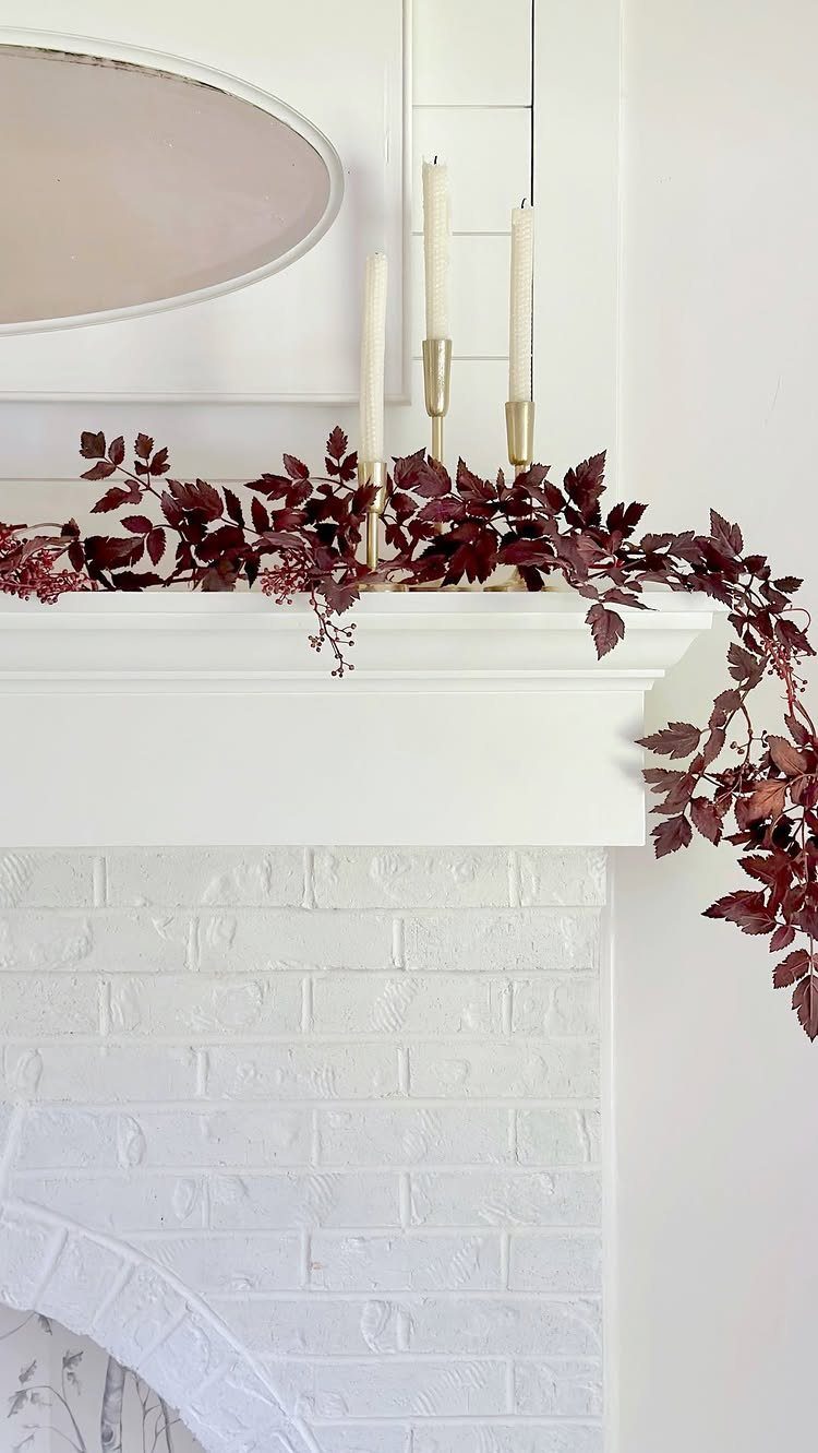 16 Fall Fireplace Mantel Decor Ideas with Photos 2 Deep red leaf garland draped across a white fireplace mantel with cream candles.
