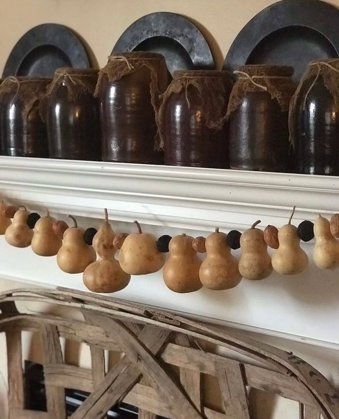 16 Fall Fireplace Mantel Decor Ideas with Photos 9 Dried gourd garland hanging from a white mantel with rustic brown ceramic jars.