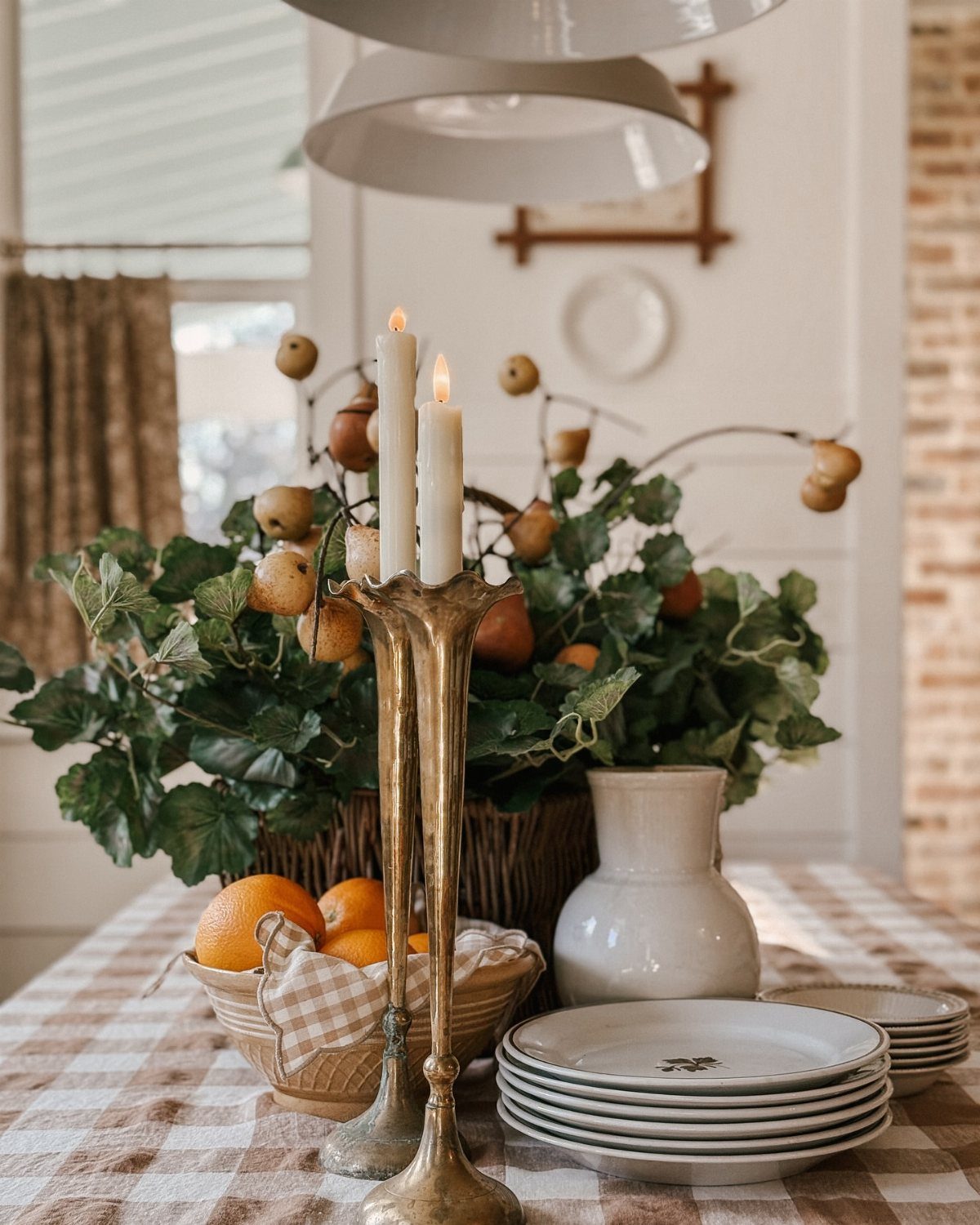 9 Farmhouse Style Dining Room Ideas with Photos 8 Dining table with checkered cloth, brass candlesticks, white plates, and greenery.