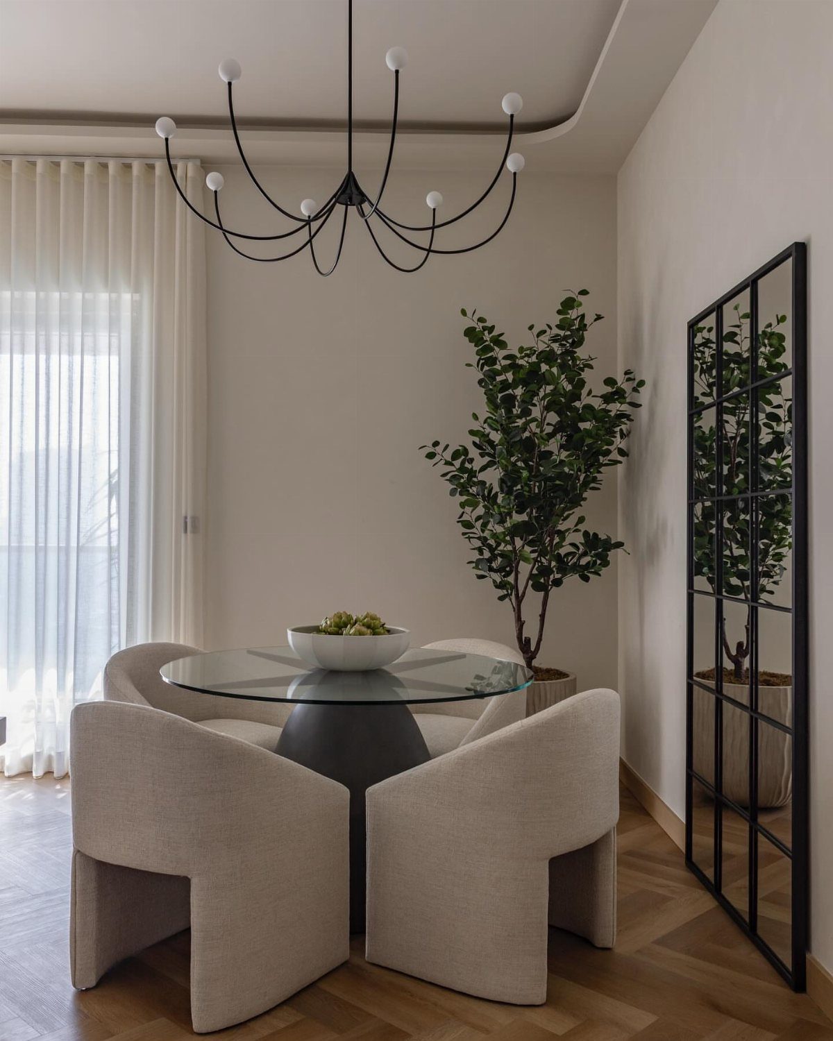 8 Feng Shui Dining Room Ideas for Balance and Flow 7 Round glass dining table with beige curved chairs and a sculptural black chandelier.