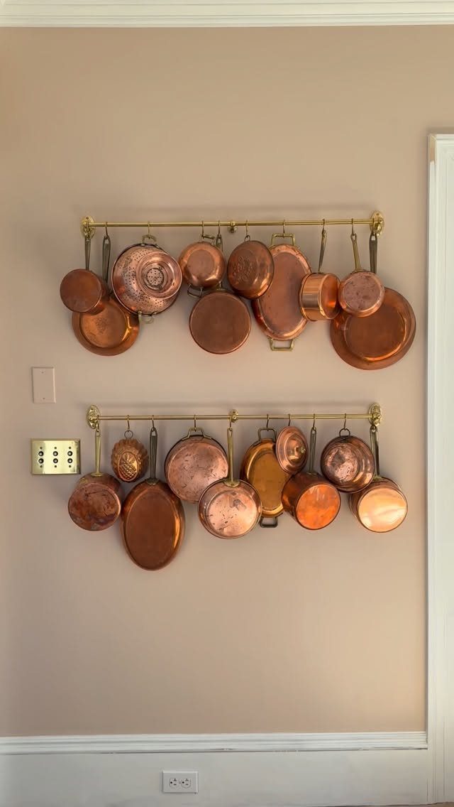 22 French Country Dining Room Ideas with Rustic Charm 19 Copper pots and pans hanging from two brass rails on a beige wall.