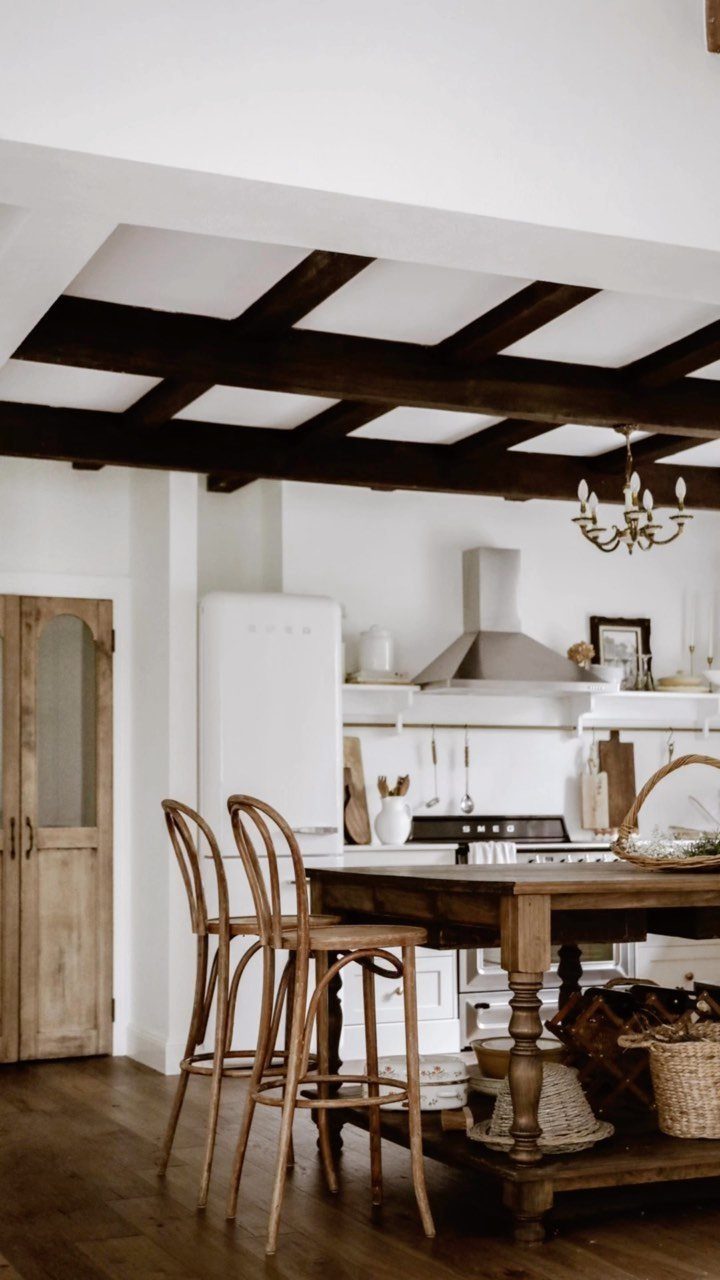 22 French Country Dining Room Ideas with Rustic Charm 14 Rustic kitchen with a wooden table, bentwood stools, and dark exposed ceiling beams.