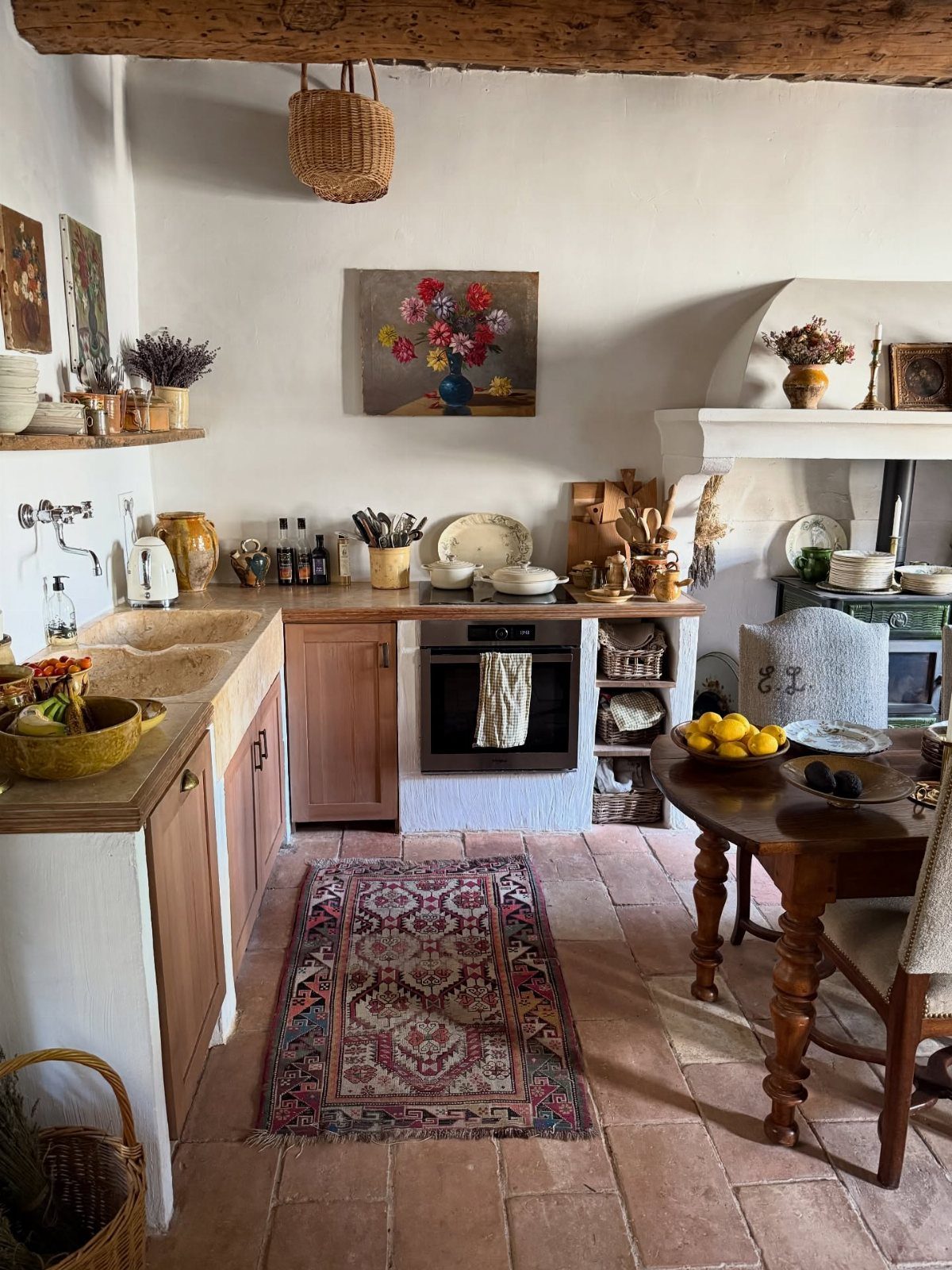 22 French Country Dining Room Ideas with Rustic Charm 7 Rustic kitchen with terracotta floors, wooden furniture, and a heavy timber ceiling beam.